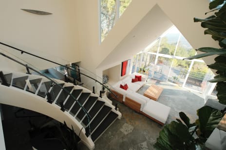 Looking down a curved white stair with black treads and curved glass railing into a bright living room.