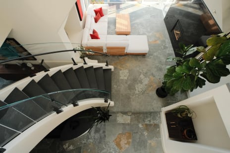 Top-down view of a curved stair with curved glass and black handrail beside a slate-floored living room.