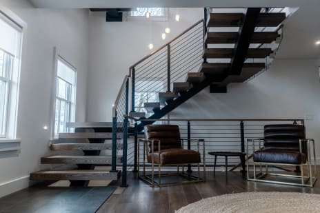 A black FLIGHT Mono switchback with dark oak treads and horizontal cable railing beside leather lounge chairs.
