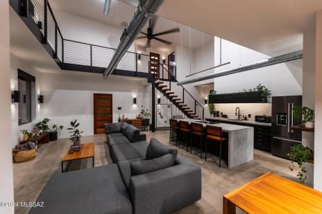 Black horizontal rod railing lines a loft and mono stair above an open living room and kitchen.