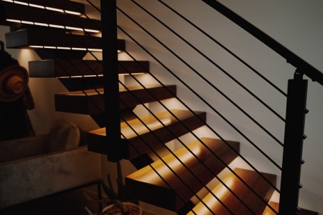 Dark wood floating treads glow with under-tread LEDs beside black horizontal rod railing in a dim room.