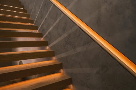 A recessed LED-lit leather handrail runs along a plaster wall above floating oak treads with warm under-lighting.