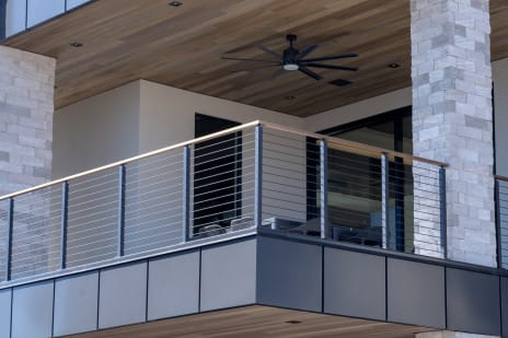 Onyx rod railing with a hardwood cap rail on a covered balcony with wood soffit and stacked-stone column.