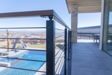 Black posts with Onyx rods and a thermally treated hardwood cap rail along a terrace above a pool.