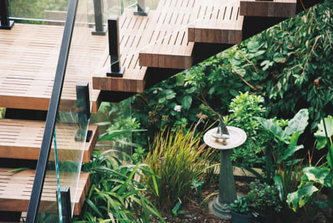 Underside view of slatted exterior treads and glass railing above a garden with a sundial.