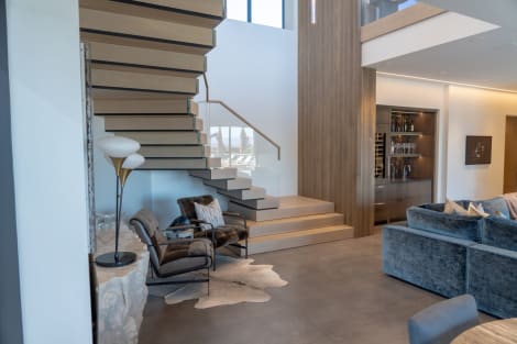 Light oak cantilevered treads rise from stacked plinth steps beside a glass railing in a modern living room.