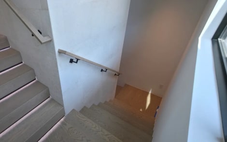 Oak stair treads with LED-lit nosings and a wall-mounted wood handrail in a stone-clad stairwell