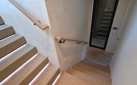 Oak stair with glowing LED tread lights and a wall-mounted handrail turning at a landing