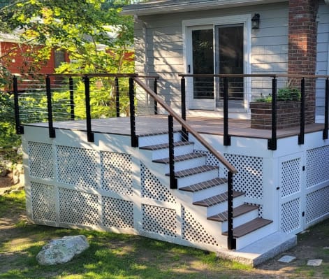 Black side-mount posts with horizontal rod infill and wood handrail around a white lattice-skirted deck and stair.