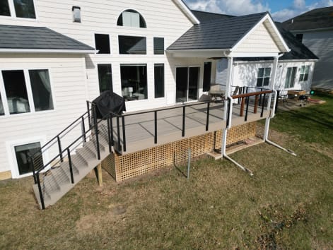 Black cable railing on a gray composite deck and stair descending to a lawn behind a white house.