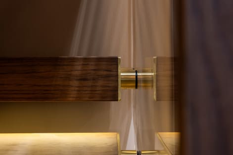 Close-up of a brass standoff pin securing glass beside a dark wood handrail with warm LED light below.