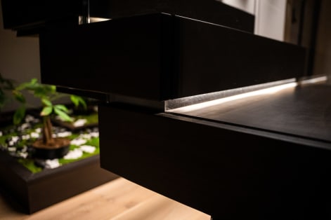 Close detail of a thick dark wood floating tread with a glowing LED strip beneath, above a small indoor garden.