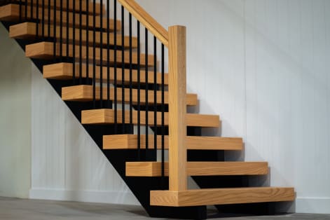 Red oak floating treads on a black stringer with black iron balusters, an oak handrail and a square oak newel against white paneling.