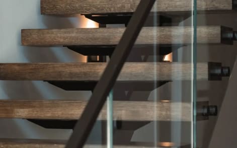 Stained oak floating treads with black standoff pins and a black handrail behind clear glass.