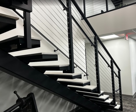 Black steel mono stair with white treads and black cable railing with wall handrail in a commercial office.