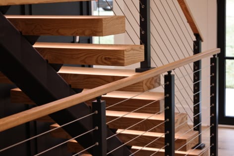 Ash floating stair with LED treads and black cable railing with an ash handrail