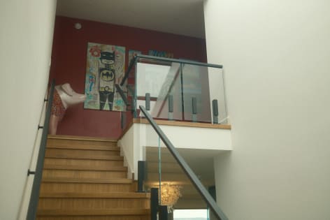 Oak stair rising to a landing with frameless glass on black talons and a black handrail against a red accent wall.