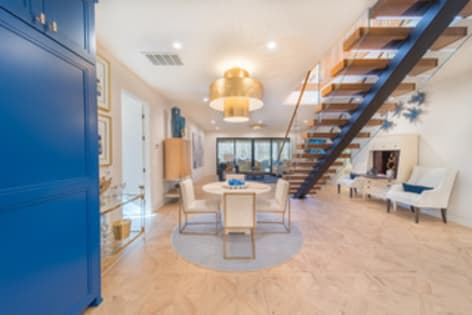 A floating wood stair with glass railing rises beside a round dining table under a gold pendant in an open room.