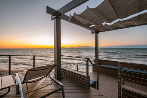 Cable railing wraps a composite deck with pergola and lounge chair overlooking the lake at sunset.