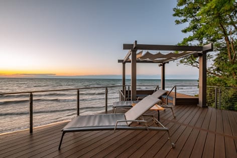 Cable railing along a composite deck with pergola and loungers above the shoreline at dusk.