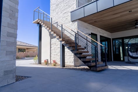 Wood treads on a steel exterior stair with black cable railing and wood handrail beside a stacked-stone column.