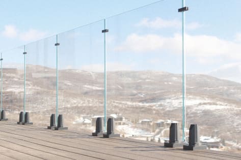 Frameless glass on black talon spigots with stabilizer clips edges a deck overlooking snowy foothills.
