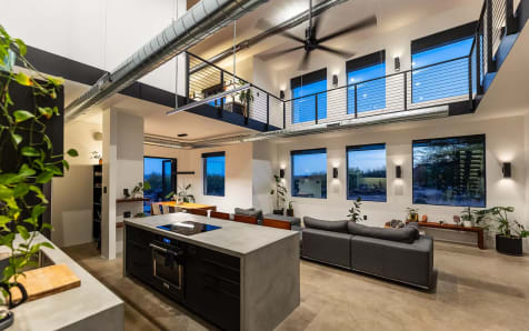 Black rod railing runs along a loft above a concrete kitchen island and living area.