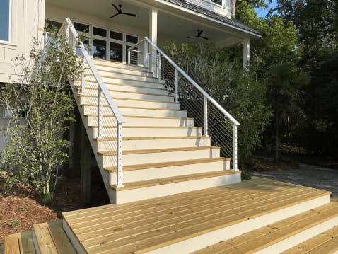 A tall exterior deck stair with white posts and stainless cables leads up to a covered porch.