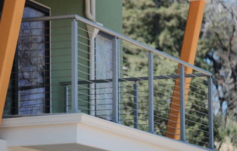 Silver cable railing on a white-trimmed balcony with orange structural braces and trees behind.