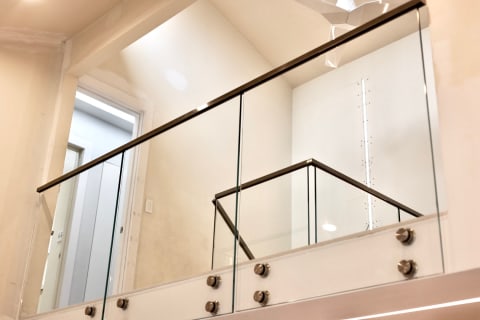 Frameless glass panels mounted on stainless standoff pins with a slim handrail line a bright upper landing.