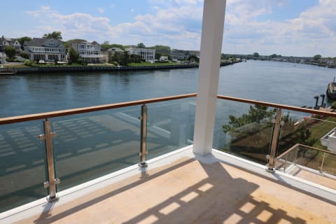 Stainless posts and a hardwood top rail frame glass panels on a balcony overlooking a calm residential waterway.