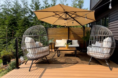 Outdoor lounge with egg chairs and umbrella on a composite deck edged by black cable railing.