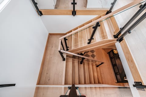 Top-down view of an oak stair turning at a landing with black side-mount glass posts and oak rails.
