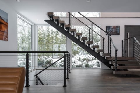 A black FLIGHT Mono with stained oak treads and cable railing rises past snow-covered windows.