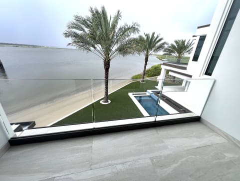 Frameless base rail glass edges a tiled terrace overlooking palms, a pool and the water