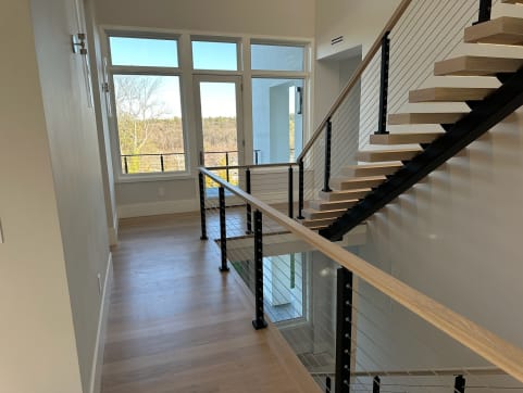 White oak treads on a black mono stringer with cable railing and oak handrail beside tall windows.