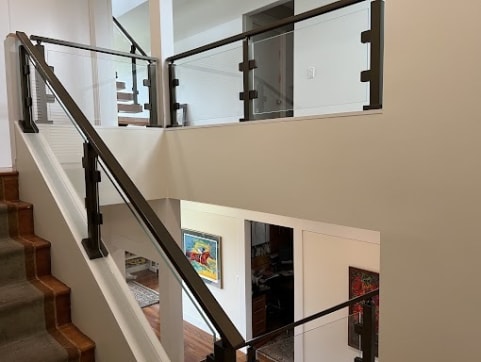 Glass panels between dark bronze posts follow a carpeted stair and wrap an upper landing.