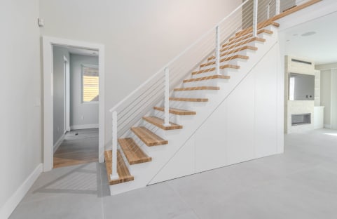 Natural oak replacement treads climb a white stair with white posts and horizontal cable railing in a bright home.