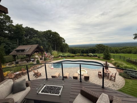 Curved composite deck with black cable railing and fire table overlooks a pool, pavilion and valley view.
