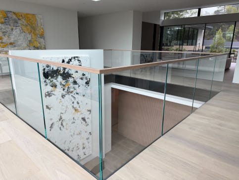 Frameless glass with a light wood cap rail surrounds a stair opening in a bright modern home.