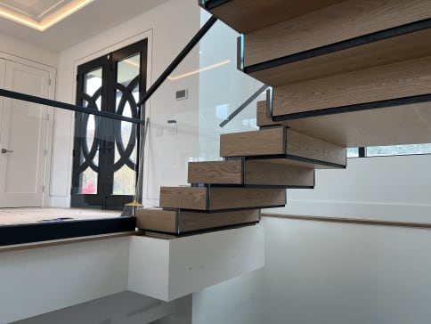 Oak Stack floating stair with a hidden built-in stringer beside frameless glass with a slim black top cap