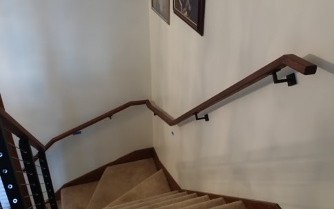Dark wood handrail on black wall-mount brackets follows a carpeted switchback stair.