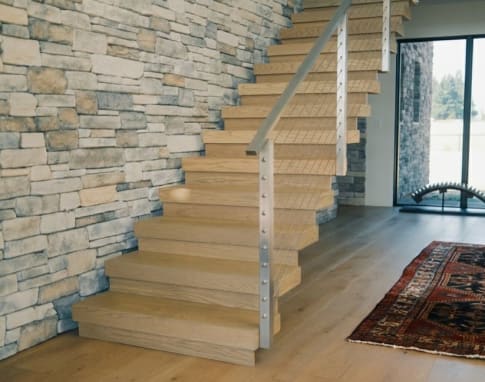 White oak stack stair with stainless cable posts rises along a stacked stone wall.