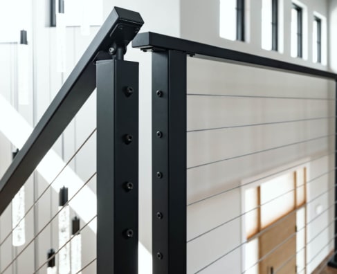 Close view of black square posts and handrail with horizontal cable infill against white shiplap.