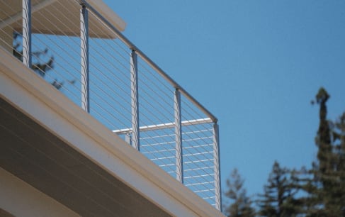 Low view up to a silver cable railing on an upper balcony against a clear blue sky.