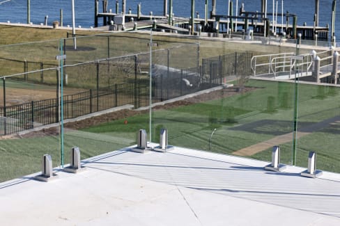 Frameless glass panels on stainless spigot clamps edge a white terrace above a lawn and marina.