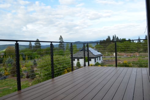 Black cable railing along a composite deck overlooking gardens and forested hills
