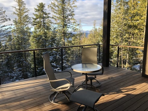 Black cable railing with wood cap around a covered deck looking out to snowy evergreens.