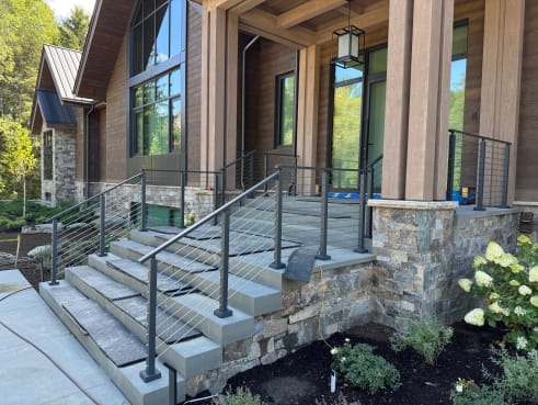 Dark posts with horizontal rod infill along stone entry steps of a timber-framed mountain home.