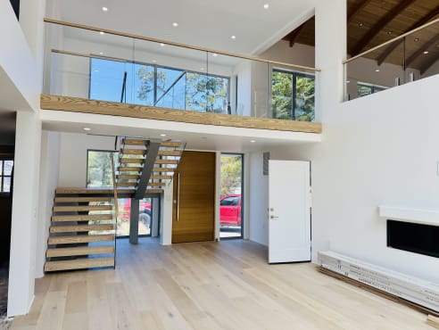 Double-height great room with a frameless glass loft railing and floating stair below
